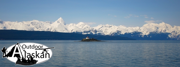 In the middle of Lynn Canal, Eldred Rock and lighthouse sit in the foreground with Sullivan Island and the Chilkat Range in the background.