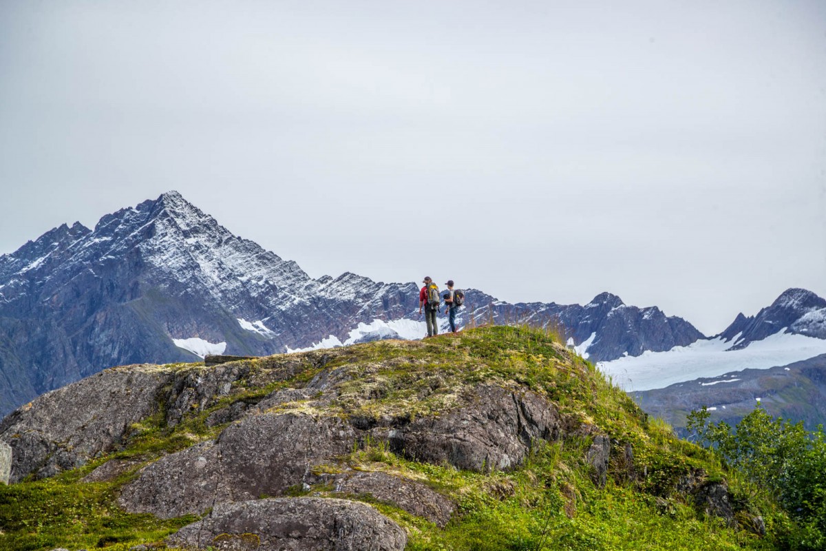 Hikers stop on a small peak to admire much larger peaks in the distance.